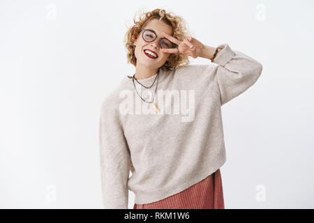 Felice entusiasta e sincera spensierata donna lgbt in bicchieri e eleganti maglione che mostra la pace o vittoria gesto vicino a occhio e sorridente largamente avente Foto Stock