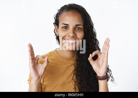 Okay, è perfetto. Felice e soddisfatto splendida afro-americano con ricci che mostra di acconciatura ok gesti con le sfere e sorridente essendo pelased con buona Foto Stock