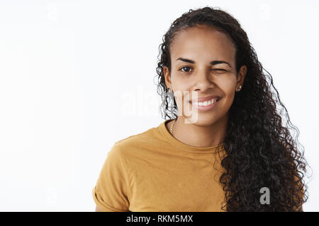 Close-up shot di optimstic e fiducioso di buona cercando di carnagione scura ragazza con capelli ricci winking in telecamera con piacere flirty sorriso controllo Foto Stock