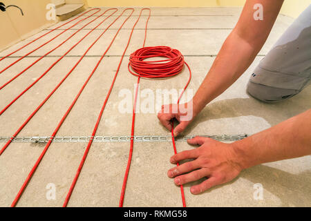 Elettricista installazione di riscaldamento elettrico rosso il filo del cavo sul pavimento di cemento in camera incompiuto. Ristrutturazione e costruzione, confortevole casa calda concep Foto Stock