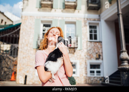 Il tema è l amicizia di uomo e animali. Giovane e bella con i capelli rossi donna caucasica tenendo un cane di razza Chihuahua in prossimità di una costruzione casa in Foto Stock