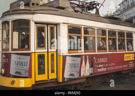 Lisbona, Portogallo - 01/03/19: Tradizionale giallo vecchio tram elettrico nel centro di Lisbona. Vista laterale con passeggeri e windows, vino Cabriz annuncio Foto Stock