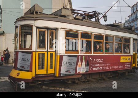Lisbona, Portogallo - 01/03/19: Tradizionale giallo vecchio tram elettrico nel centro di Lisbona. Vista laterale con passeggeri e windows, vino Cabriz annuncio Foto Stock