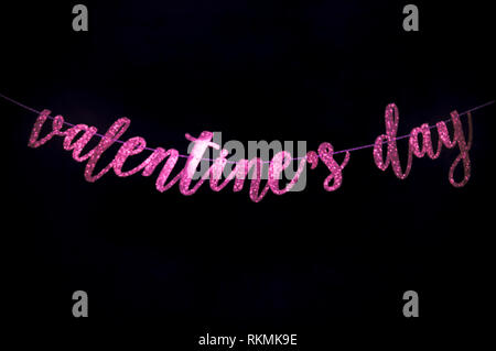 Sfocati Romantico San Valentino messaggio in spumante rosa manoscritta script banner appesi attraverso uno scuro su sfondo nero Foto Stock