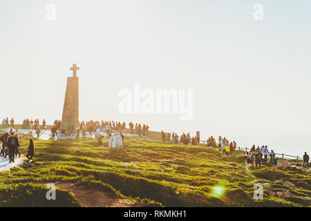 Sintra, Portogallo - 01/05/19: le persone a bordo dell' Europa al tramonto, Capo Roca, oceano, un sacco di gente, sun flare, molto luminoso. Una croce cristiana. Foto Stock