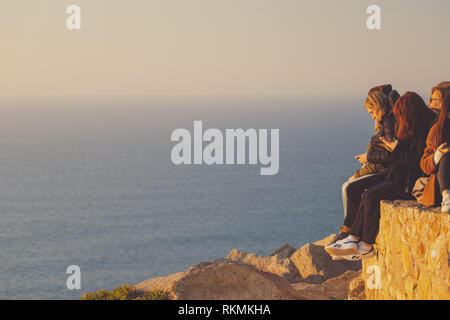 Sintra, Portogallo - 01/05/19: persone in piedi sul bordo dell'Europa tramonto, Cape roca. Europeo occidentale. Persone appeso su una rupe enorme Foto Stock