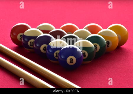 Numerate palle da biliardo con due stecche da biliardo su un feltro rosso tabella. Foto Stock