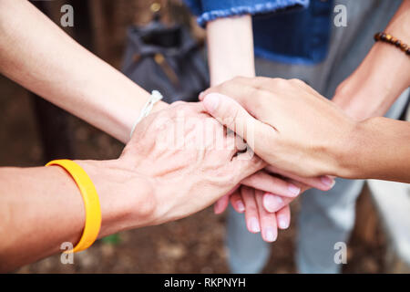 Giovani uomini e donne in piedi e mani di impilaggio in una riunione sul suolo naturale background in gita all'aperto. Il lavoro di squadra, la diversità, la collaborazione dei giovani Foto Stock