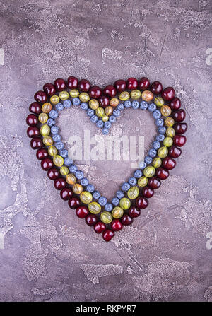 Fresche ciliege dolci, mirtillo e goosberry in forma di cuore oltre sul cemento grigio. Vista dall'alto. Copia dello spazio. Foto Stock