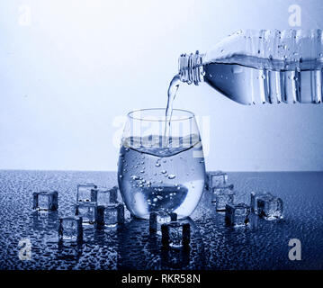 Versando potabile fresca acqua minerale dalla bottiglia di plastica. Di vetro riempita con acqua su sfondo bianco. Foto Stock