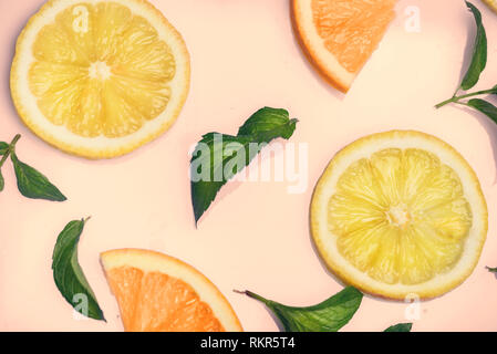 Fette di agrumi e di erbe di menta modello sul retro sfondo rosa dal di sopra. Vista dall'alto di arancia e di limone fette di frutta su sfondo color pastello. Foto Stock