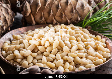 I pinoli nella ciotola e pinoli coni del tavolo di legno. Alimenti biologici. Foto Stock