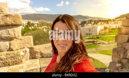 Ritratto di un normale brunette adolescente hipster con gli occhiali e bretelle sorridente e prendendo un selfie. Viaggiare a bodrum, Turchia. Foto Stock