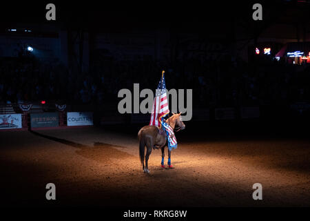 Giovane donna americana di equitazione al rodeo e azienda noi bandiera per l'inno nazionale in Cowtown Coliseum, arena di stockyards di Forth Worth, Te Foto Stock