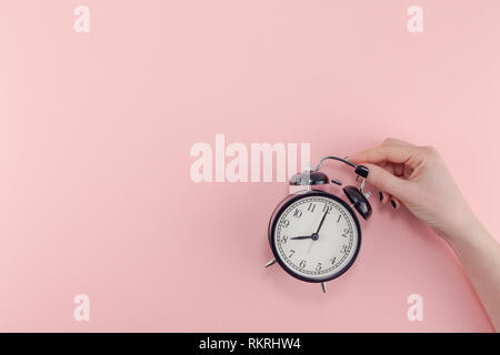 Creative laici piatto mattina tempo emozioni concetto vista superiore della donna mano azienda annata nera sveglia pastello rosa millenario Colore sfondo della carta Foto Stock