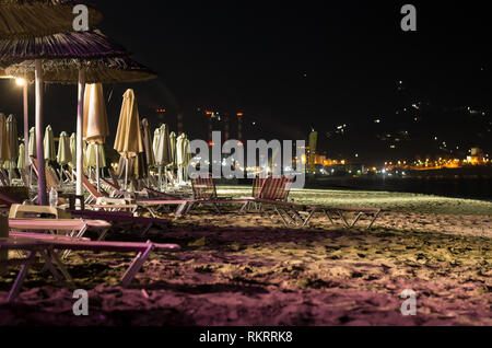 Paesaggio notturno con una spiaggia deserta con ombrelloni e sedie a sdraio e illuminazione notturna (Amoudara, Grecia) Foto Stock