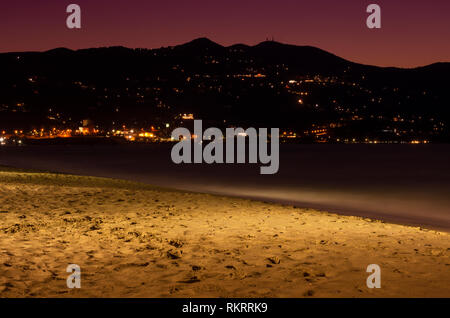 Di notte le luci di un paese di montagna vicino alla spiaggia della Baia di Heraklion in Grecia dopo il tramonto Foto Stock
