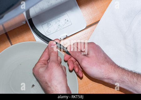 Il maestro esegue la manutenzione della lavatrice. Pulizia del filtro, tenendo un tubo flessibile, tubo nero Foto Stock