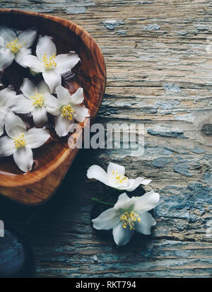 Wellness e Spa sfondo vintage. Jasmin petali di fiori in legno di bambù ciotola con acqua. Il relax e la cura del corpo concetto. Foto Stock