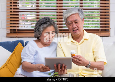 Asian coppia senior utilizzare computer tablet ricerca medico pillola seduti sul divano di casa,senior imparare a utilizzare la tecnologia Foto Stock