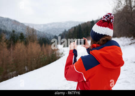 Giovane donna in escursionismo marcia di scattare una foto di un paesaggio invernale con il suo cellulare mentre sono fuori per una escursione Foto Stock