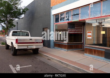 Old Ford pickup truck vicino negozio chiuso in Winslow, Arizona, Stati Uniti d'America. Negozio con in vendita e in affitto segno e bandiera americana sul windo Foto Stock