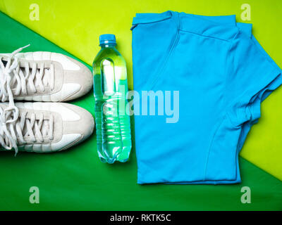Appartamento giaceva sul green sport mat sfondo di sport t-shirt, pantaloni, bianco sneaker, voci di fitness, vista dall'alto Foto Stock