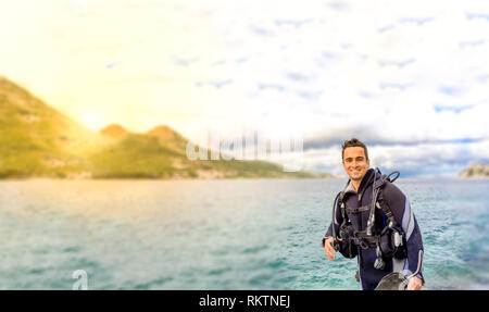 Giovane uomo bello isolato diver sorridente pronto a fare immersioni in acqua fredda muta, alette, peso belt & oxigen ingranaggio in Karaburun, Izmir. Turchia Foto Stock