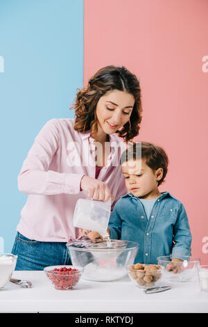 Piuttosto la mamma con carino piccolo figlio di setacciare la farina di ciotola insieme sullo sfondo bicolore Foto Stock