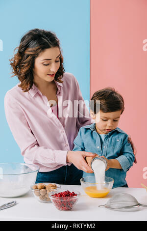 Madre aiutare piccolo figlio di aggiunta di zucchero alla panna uova su sfondo bicolore Foto Stock