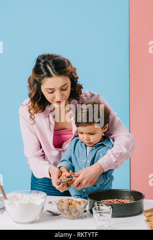 Madre aiutare piccolo figlio di noci di cracking per pasticceria su sfondo bicolore Foto Stock