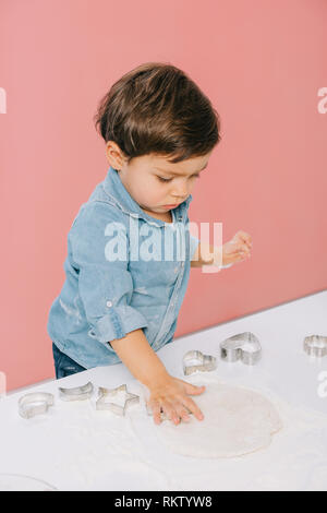 Little Boy taglia le figure in pasta con la pasta stampi isolato in rosa Foto Stock