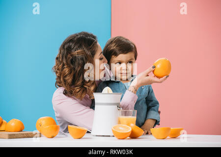 Madre che mostra tutto il succo di arancia di carino piccolo figlio su sfondo bicolore Foto Stock