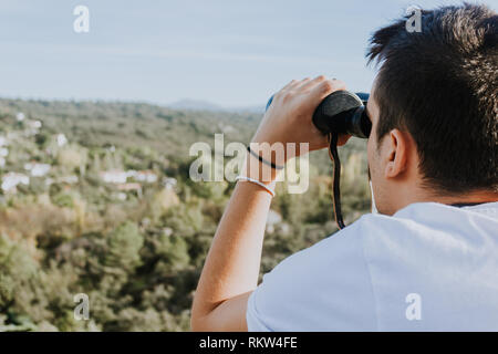 Un uomo che guarda attraverso il binocolo sulla montagna in estate Foto Stock