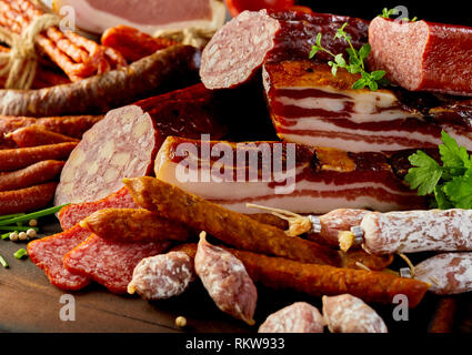 Selezione di specialità salsicce piccanti, salame affumicato e lardo visualizzata su un tavolo di legno con erbe fresche e grani di pepe in una vista ravvicinata Foto Stock