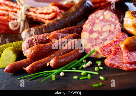 Un assortimento di piccante salsiccia conditi con erba cipollina fresca, cetriolo sottaceto o cetriolino e grani di pepe su di un tavolo di legno in una vista ravvicinata Foto Stock