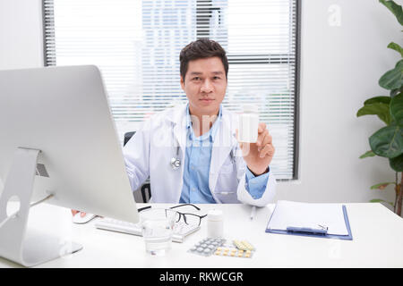 Medicina medico medico o farmacista seduti a tavola portapezzo, azienda o mostra una bottiglia di pillole in mano sul modulo speciale. Cure mediche, farmacia o egli Foto Stock