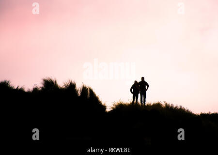 Persone stagliano contro la luce della sera come stanno tra l'erba marram sulle dune a Crantock Beach in Newquay in Cornovaglia. Foto Stock