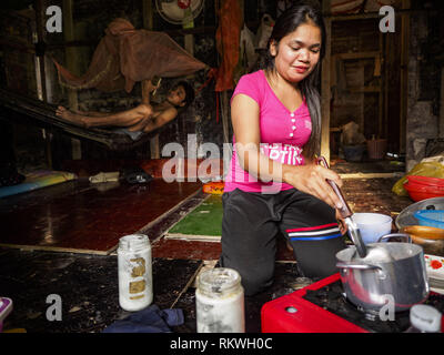 Sihanoukville, Preah Sihanouk, Cambogia. 12 Feb, 2019. La moglie di un cambogiano lavoratore edile (in amaca in background) rende la cena nella loro casa in Blue Bay casino e resort, un progetto cinese in Sihanoukville. Ci sono circa 50 casinò cinese e resort hotel aperto o in costruzione in Sihanoukville. I CASINÒ sono cambiando la città, una volta che una sonnolenta porta sul sudest asiatico del ''backpacker trail'' in una fiorente città. Il cambiamento è in arrivo con un costo però. Molti residenti cambogiano di Sihanoukville hanno perso le loro case per fare la strada per il casinò e la jo Foto Stock