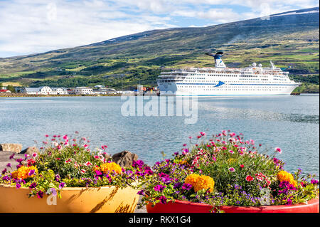 Akureyri, Islanda - 17 Giugno 2018: villaggio di pescatori town harbour marina con la nave di crociera in barca e fiordo con montagne e vasi di fiori Foto Stock