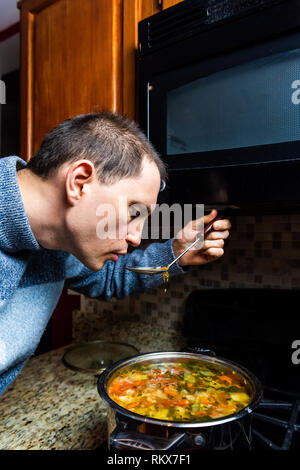 Verticale Closeup Ritratto di giovane uomo degustazione di cucina casalinga invernale calda zuppa di verdure con siviera in maglione a freddo Foto Stock