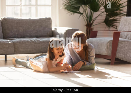 Happy mom aiutare bambino ragazza disegno sul pavimento caldo insieme Foto Stock