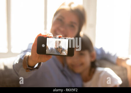 Felice madre abbracciando bambino figlia tenendo il telefono tenendo selfie Foto Stock