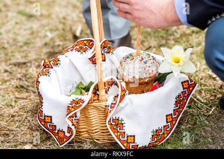 Kulich tradizionale ortodossa ucraina benedizione pasquale in vimini cesto di paglia con uomo candela di illuminazione sul terreno di erba al di fuori della chiesa con le mani Foto Stock