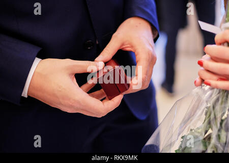 Un uomo in tuta blu contiene un piccolo regalo in legno box di anelli di nozze. regalo di nozze Foto Stock