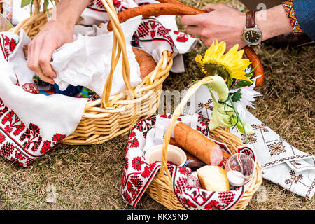 Il Russo Ortodosso Ucraino benedizione pasquale in vimini cesto di paglia con la persona che effettua la salsiccia di carne di erba sul terreno al di fuori della chiesa con fiori Foto Stock