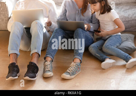 I genitori tenendo i laptop seduto sul pavimento con capretto telefono azienda Foto Stock