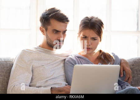 Confuso perplesso moglie e scioccato frustrato marito la lettura di notizie online Foto Stock