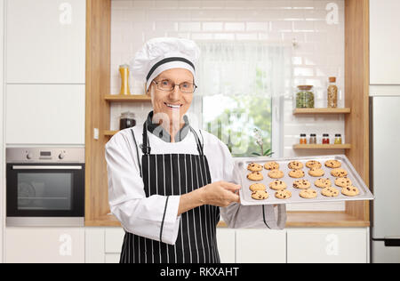 Anziani baker tenendo un vassoio con biscotti appena sfornati in una cucina Foto Stock