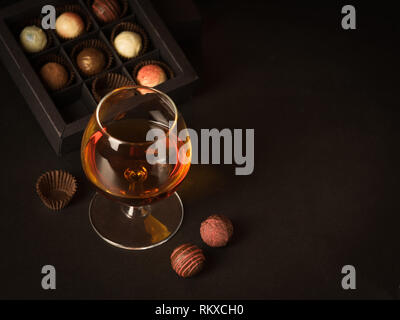 Un bicchiere di brandy cioccolato e caramelle su uno sfondo scuro. La bevanda alcolica e cioccolato elite concetto alimentare. Foto Stock